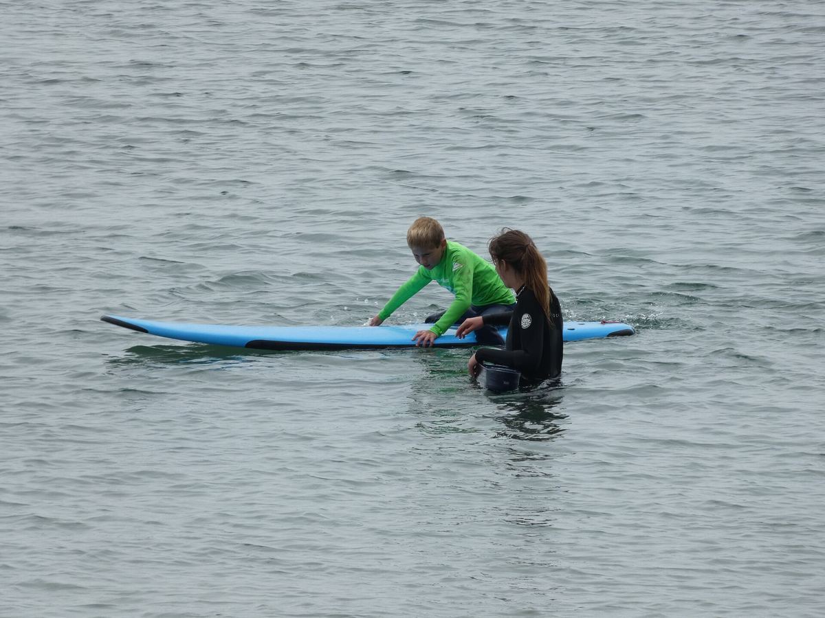 Surf coach in the water steadying a beginner lying on a soft-top board